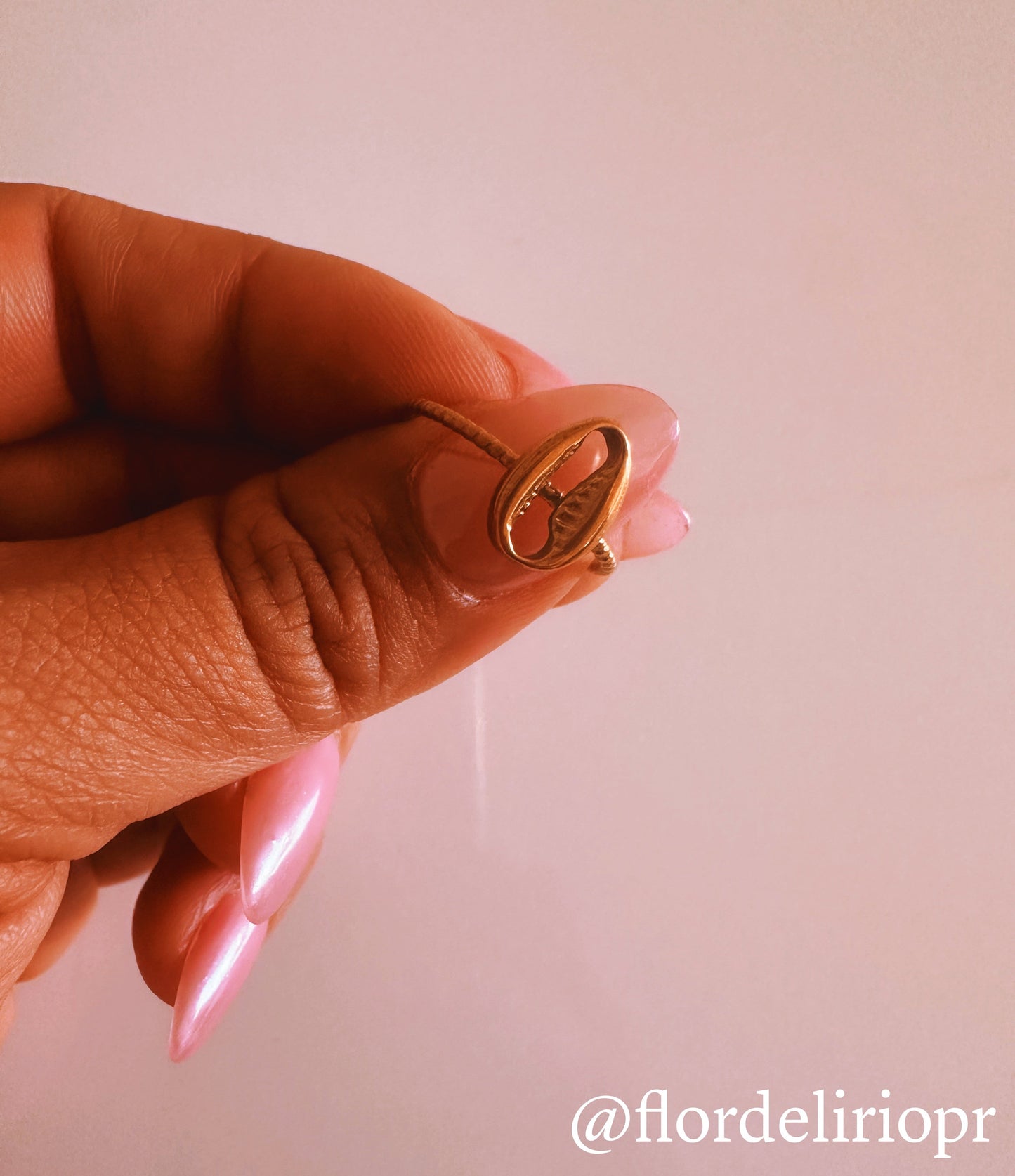 Adjustable 18k gold plated beach shell ring with a smooth, shiny finish held between fingers with pink nails.